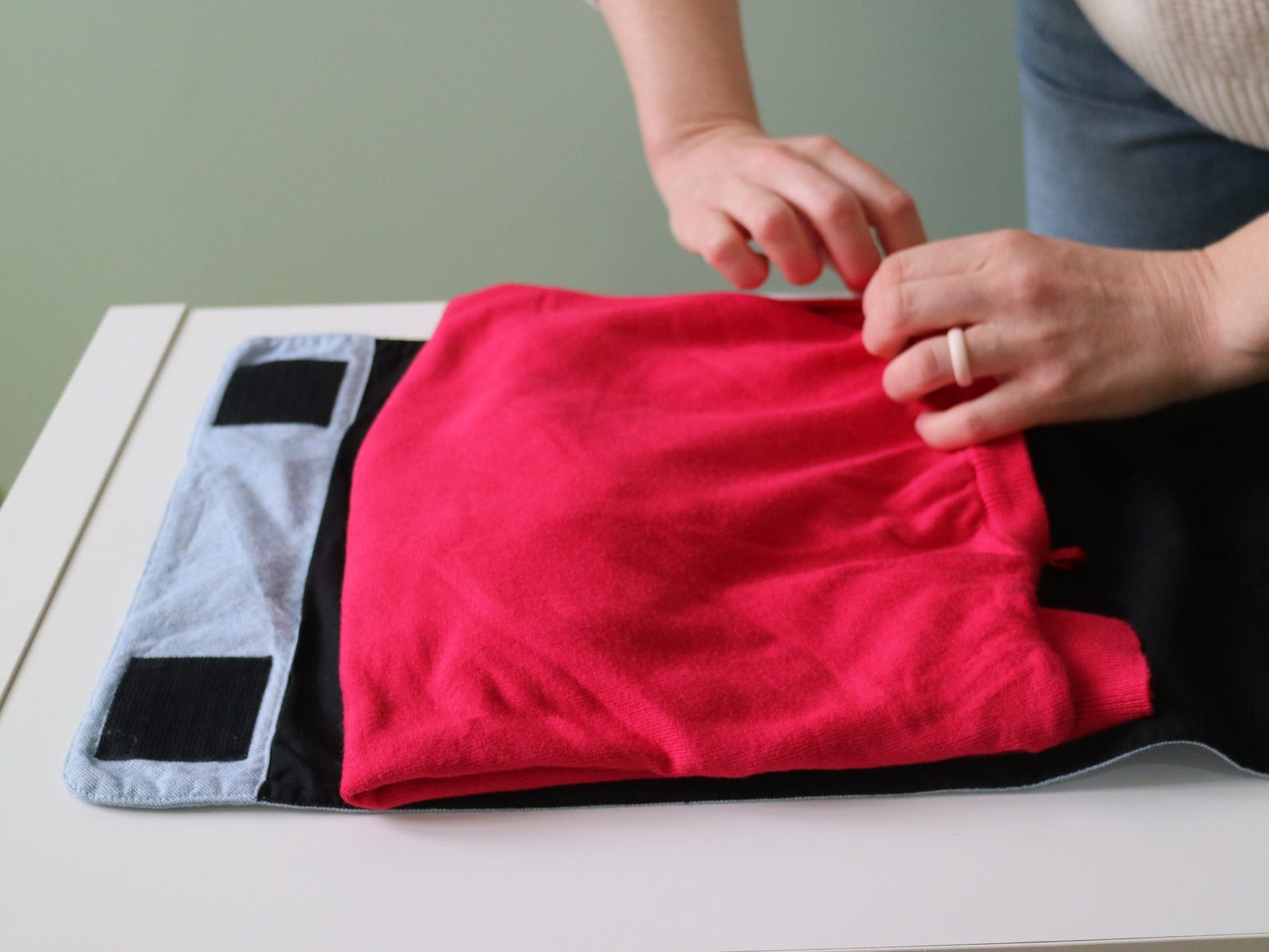 Hands place a folded sweater onto the Furl, leaving the Velcro patches uncovered.