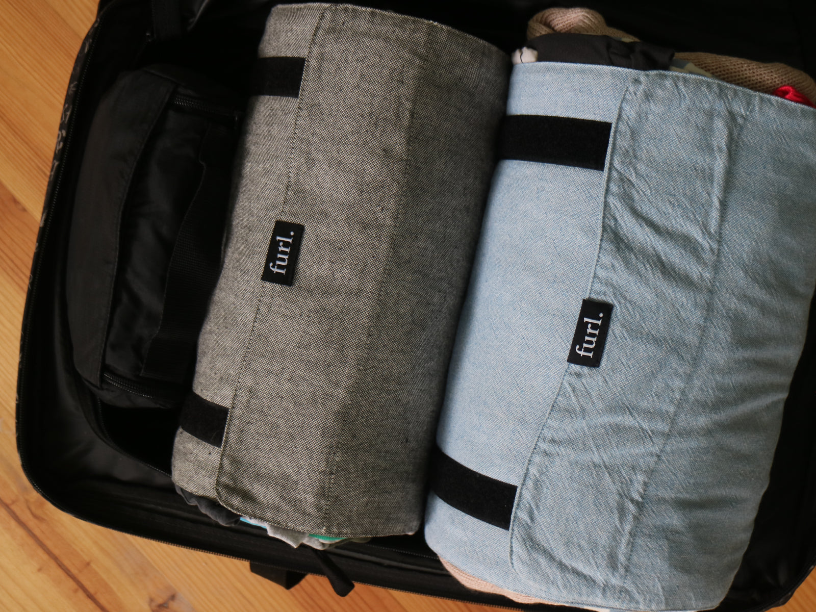 An open suitcase containing two rolled Furls and a toiletry bag.